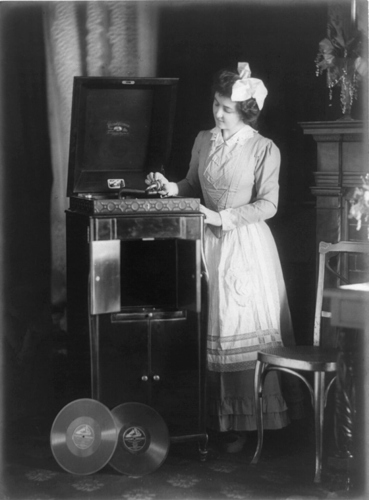 Woman%2C_with_large_bow_in_her_hair%2C_putting_needle_on_record_on_phonograph
