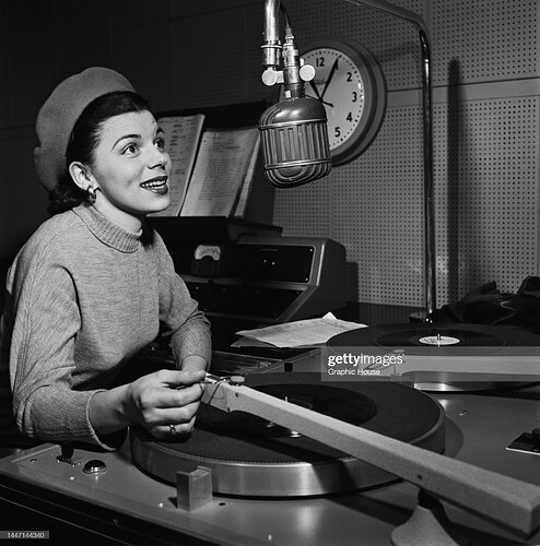 An unspecified female radio disc jockey, wearing a turtleneck sweater and a beret, holding the tonearm of a turntable in an unspecified radio studio, location unspecified, location unspecified, United States, circa 1955 2