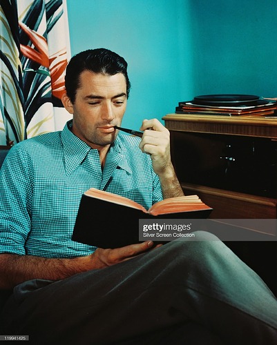 Gregory Peck (1916-2003), US actor, smoking a pipe while reading a book, while listening to records playing on a turntable beside him, circa 1955. (Photo by Silver Screen CollectionGetty Imag